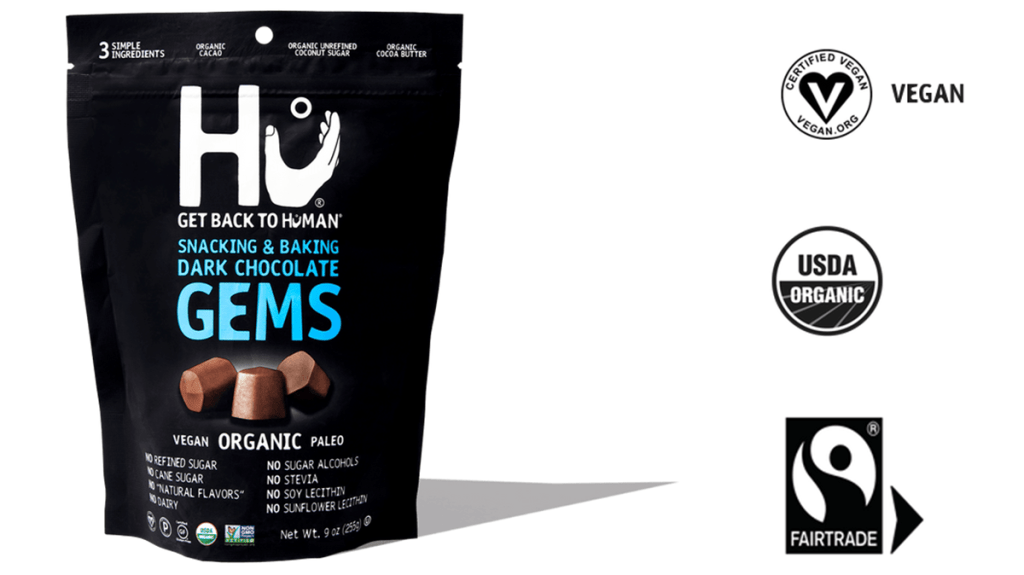A bag of Hu Dark Chocolate Gems is pictured next to three logos indicating key certifications: vegan, organic, and fair trade.